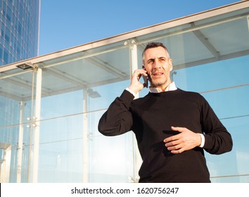 Handsome Silver Fox Man Talking On Mobile Phone With Glass Office Building In Background 