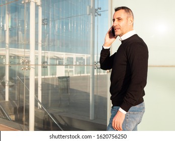 Handsome Silver Fox Man Talking On Mobile Phone With Glass Office Building In Background 