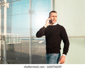 Handsome Silver Fox Man Talking On Mobile Phone With Glass Office Building In Background 