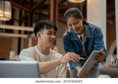 A handsome, smart Asian man is working with his female colleague, reviewing her work on a digital tablet and offering advice and ideas. teamwork, college students, colleagues - Powered by Shutterstock