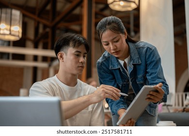 A handsome, smart Asian man is working with his female colleague, reviewing her work on a digital tablet and offering advice and ideas. teamwork, college students, colleagues - Powered by Shutterstock