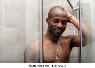 handsome smiling african american man with closed eyes taking shower