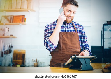 Handsome Smiling Barista With Beard Taking Order On Cell Phone And Using Tablet In Cafeteria