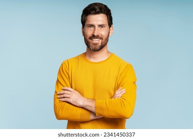 Handsome smiling bearded man wearing t shirt looking at camera isolated on blue background. Confident modern hipster with stylish hair after barbershop service