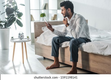handsome and smiling bi-racial businessman using smartphone in morning at home - Shutterstock ID 1591198141