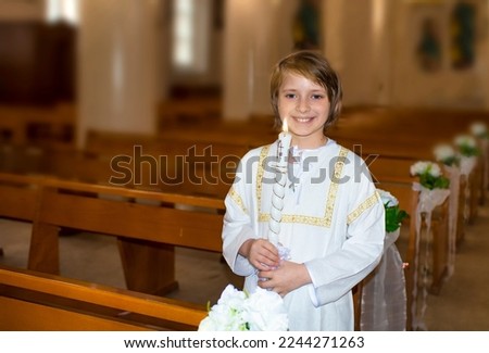 a handsome smiling boy in white clothes with a church candle stands in a Catholic church after baptism or before the feast of the first communion.