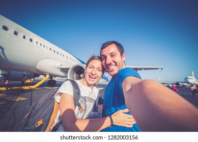 gut aussehendes, lächelndes Paar, das bereit ist, im Flughafen zu fliegen, Sommerferien und Reisen um die Welt, Blick auf das Flugzeug im Hintergrund