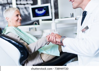 Handsome Smiling Dentist Looking At X-ray Image Of His Senior Woman Patient. 