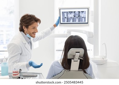 Handsome smiling dentist showing his patient x-ray results, on modern lcd display in modern dental office - Powered by Shutterstock