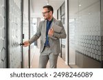 Handsome smiling entrepreneur holding laptop and opening glass door of board room in modern office