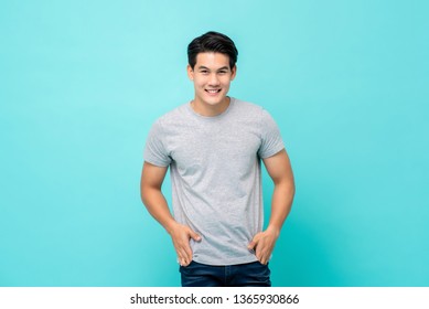 Handsome Smiling Friendly Asian Man In Casual Plain T-shirt With Hands In Pockets On Light Blue Background