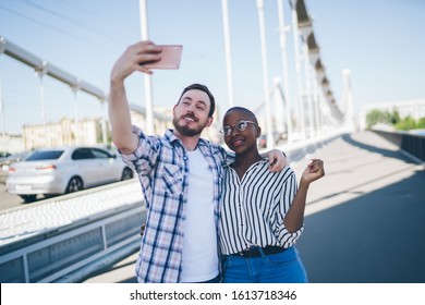 Handsome Smiling Guy In Shirt With Sleeves Rolled Up Using Cellphone For Selfie Hugging African American Sensual Female With Short Hair Strolling In Street