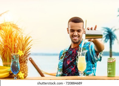 Handsome smiling Latin American bartender standing near the bar counter, preparing cocktail and adding something in the glass at the resort in rays of the sun. Concept of preparation, relaxing and fun - Powered by Shutterstock