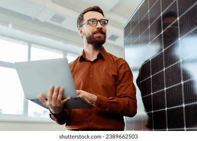 Handsome smiling man, engineer, developer holding laptop computer planning startup working with solar panel in modern office. Innovation, renewable energy concept  - Powered by Shutterstock