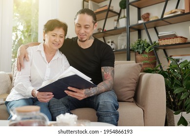 Handsome Smiling Man Hugging His Mature Mother When They Are Looking At Old Photos In Album