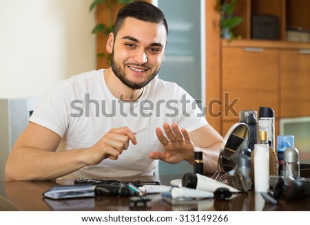 Handsome smiling metrosexual guy doing manicure at home