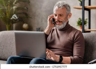 Handsome Smiling Middle Aged Businessman Talking On Mobile Phone And Using Laptop While Working At Home