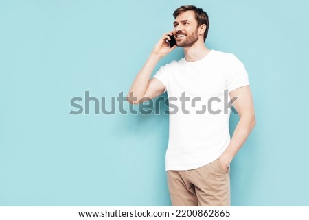 Handsome smiling model.Sexy stylish man talking at smartphone. Fashion hipster male posing near blue wall in studio. Holding phone. With cellphone