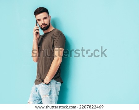Handsome smiling model.Sexy stylish man talking at smartphone. Fashion hipster male posing near blue wall in studio. Holding phone. With cellphone. Isolated