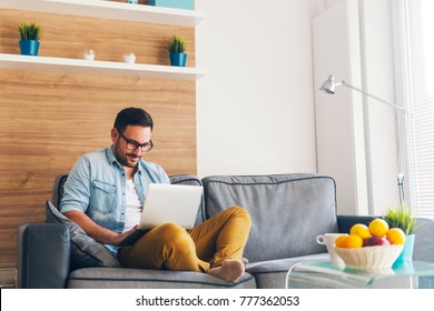 Handsome Smiling Modern Man Relaxing On Couch And Using Laptop