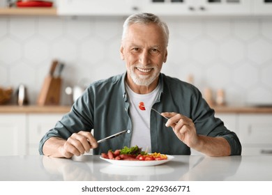 Handsome Smiling Senior Man Eating Tasty Meal In Kitchen At Home, Happy Elderly Gentleman Sitting At Table And Looking At Camera, Enjoying Delicious Food, Holding Fork And Knife, Copy Space - Shutterstock ID 2296366771