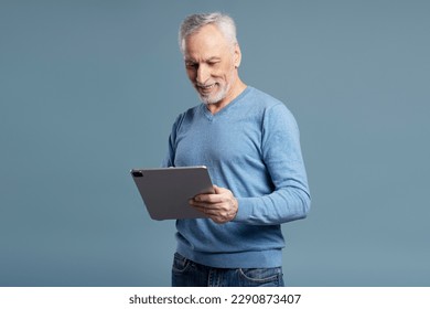 Handsome smiling senior man holding digital tablet shopping online isolated on blue background. Happy 60 years old male watching videos, reading e book. Technology concept   - Powered by Shutterstock