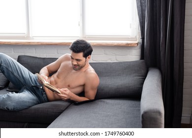 handsome smiling shirtless man reading book on sofa