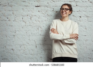 Handsome smiling woman hipster wearing blank sweater and eye glasses. White bricks wall background