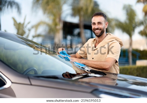 Handsome smiling worker cleaning car\
using micro fiber cloth. Car washing service\
concept\

