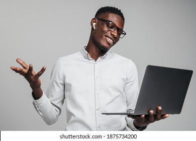 Handsome Smiling Young African Business Man Holding Laptop Computer Isolated Over Gray Background, Talking With Colleagues Via Video Call