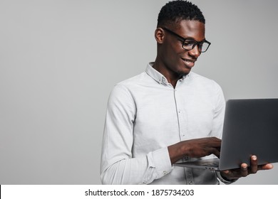 Handsome smiling young african business man using laptop computer isolated over gray background, wearing white formal shirt