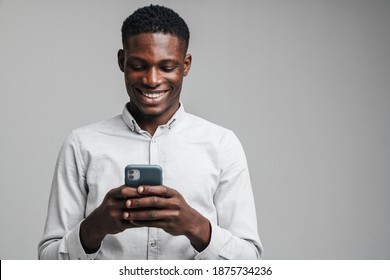 Handsome Smiling Young African Business Man Using Mobile Phone Isolated Over Gray Background, Wearing White Formal Shirt