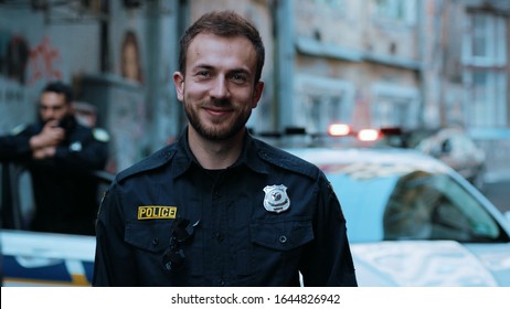 Handsome Smiling Young Man Cops Stand Near Patrol Car Look At Camera Enforcement Officer Police Uniform Auto Safety Security Communication Control Policeman Close Up Slow Motion