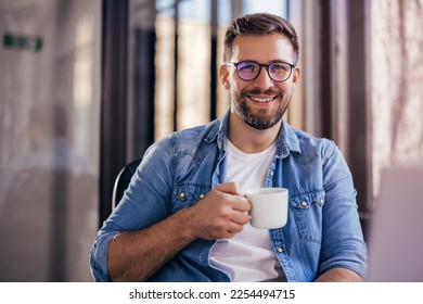 Handsome smiling young man drinking coffee sitting at office desk and looking at camera - Powered by Shutterstock