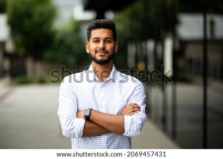 Handsome smiling young man with folded arms. Beautiful portrait of laughing joyful cheerful men with crossed hands in a city
