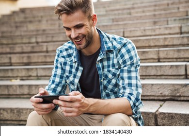 Handsome smiling young man using mobile phone while sitting on steps outdoors