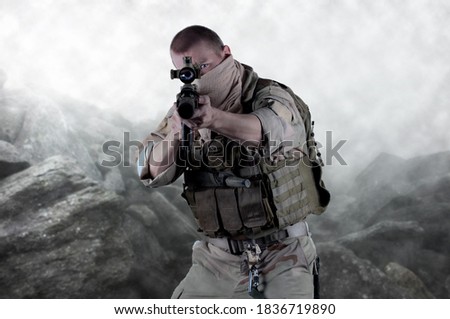 Handsome sniper looking through the scope of his rifle with his eyes visible on lens. He wears tactical vest with some extra pouches, army uniform, his sleeves are rolled up. 