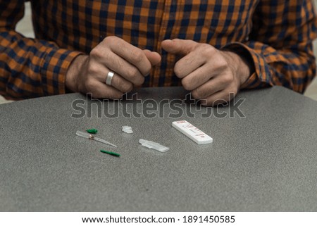 
A handsome, solid curly-haired man in a plaid shirt makes a rapid test for antibodies to coronavirus covid 19 at home. He opened a rapid test kit, pricked his finger, and tested for Ig G and Ig M.
