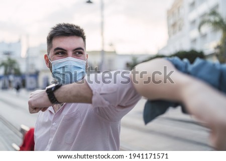 A handsome Spanish man wearing a mask and greeting his friend with elbows - new normal concept