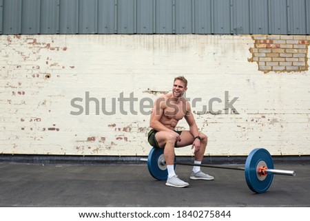 Handsome sportive man sitting on barbells, resting after workingout