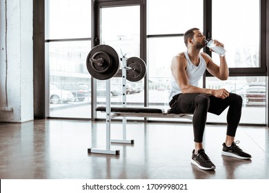 handsome sportsman drinking protein milkshake near barbell in gym