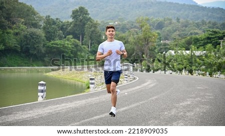 Handsome and sporty fit millennial Asian man in sportswear running along the lake, jogging in the morning. Healthy lifestyle concept