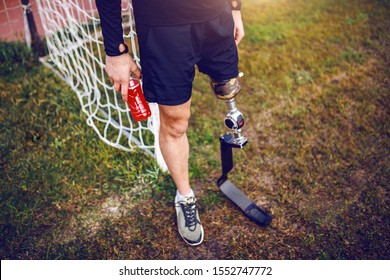 Handsome sporty handicapped man in sportswear and with artificial leg while standing on football court and holding refreshment. - Powered by Shutterstock