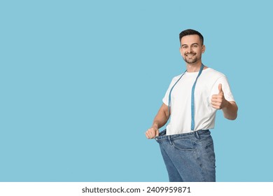 Handsome sporty young man in loose jeans with measuring tape showing thumb-up gesture on blue background. Weight loss concept - Powered by Shutterstock