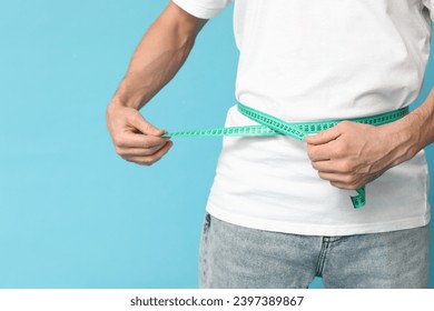 Handsome sporty young man measuring his waist on blue background, closeup. Weight loss concept - Powered by Shutterstock