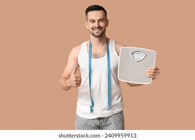 Handsome sporty young man with scales and measuring tape showing thumb-up gesture on brown background. Weight loss concept - Powered by Shutterstock