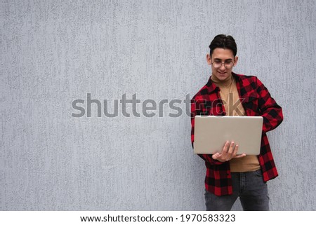 Handsome student with laptop points with gestures to the side. Boy in a red plaid shirt. Exclusive, offer and promotion.