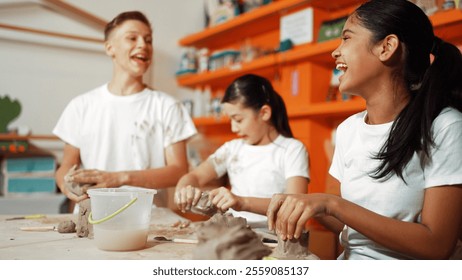 Handsome student playing with friend while put the clay on shirt at class. Group of diverse children working or modeling vase. Happy boy put water to young girl while laugh with happy. Edification. - Powered by Shutterstock