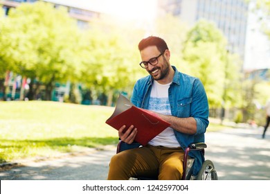 Handsome student in a wheelchair looking at a book and studying outside.