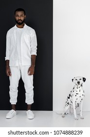 Handsome Stylish African American Man In White Clothes With Dalmatian Dog Near Black And White Wall